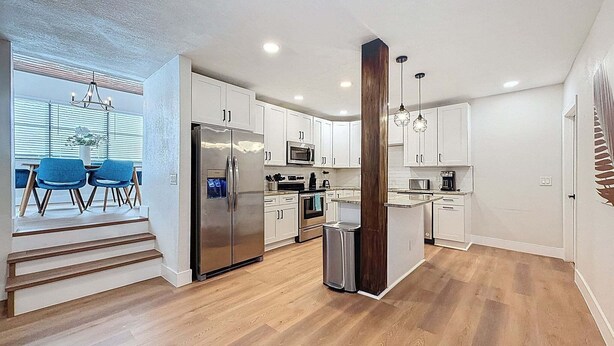 A modern kitchen with white cabinets, stainless steel appliances, and a wooden accent column.