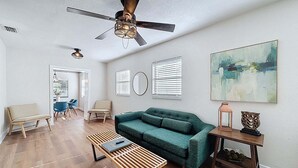 A living room with a green sofa, a wooden coffee table, a ceiling fan, and a painting on the wall.