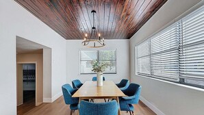 A dining area with a wooden table, blue chairs, a chandelier, and a view through window blinds.
