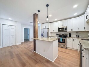 Une cuisine moderne avec des armoires blanches, un îlot central, des appareils en acier inoxydable et un mur d’accent en bois.