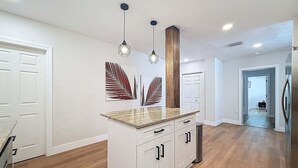 A modern kitchen with white cabinetry, a granite countertop, pendant lighting, and a wooden accent column.