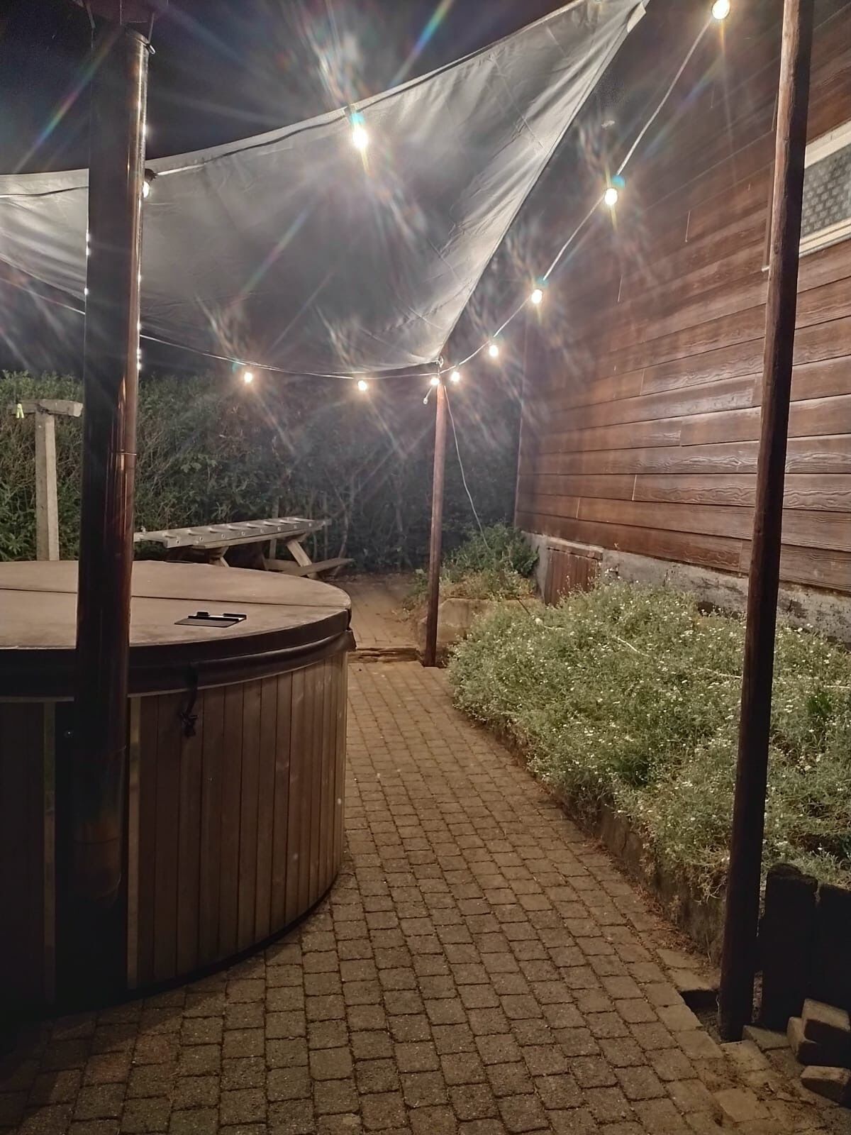 Uma área de estar ao ar livre com hidromassagem, luzes de fada e um deck de madeira.