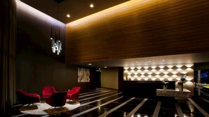 A modern lobby with a reception desk, red chairs, and a geometric patterned wall.