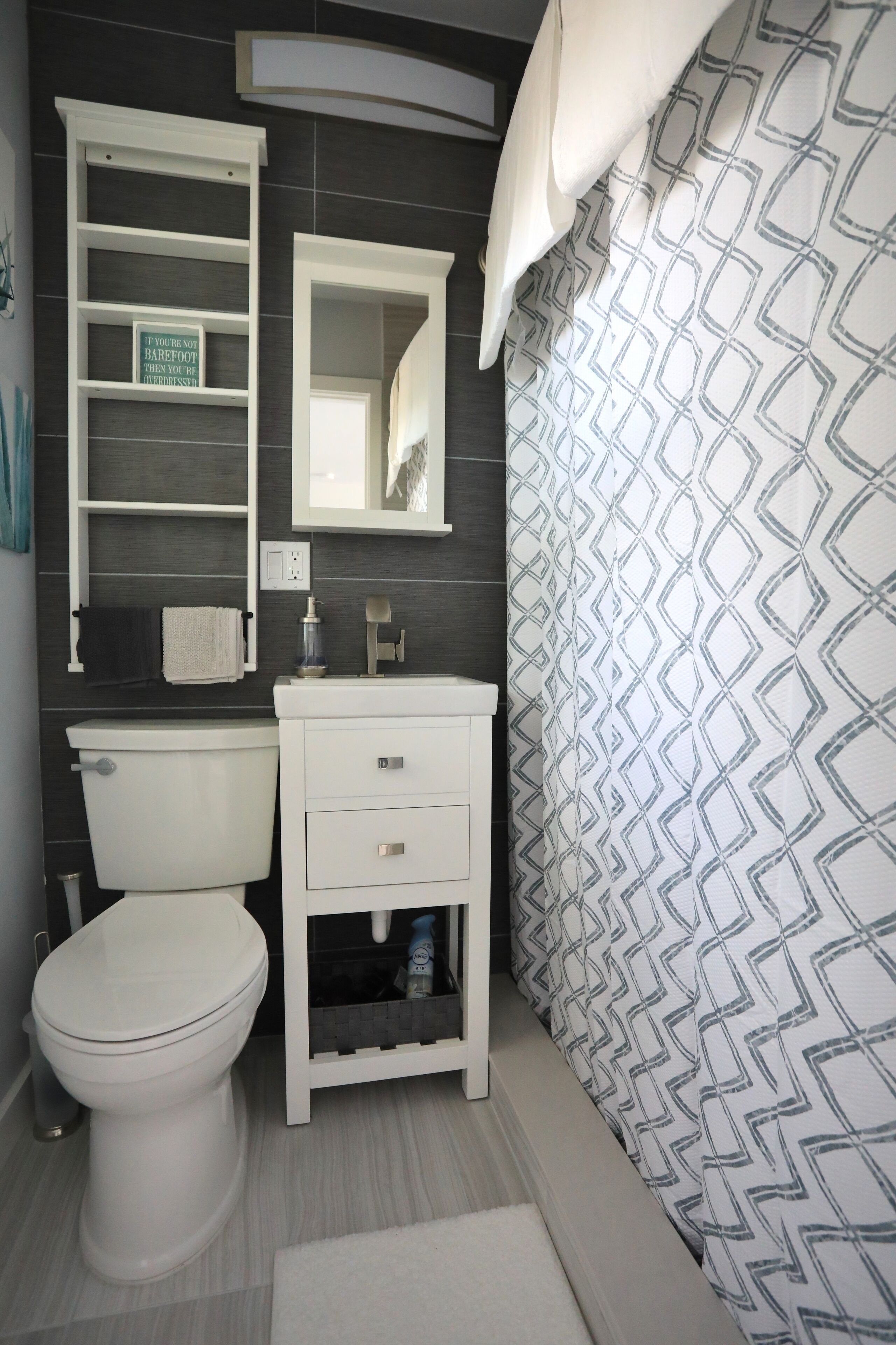 Une salle de bain comprenant des toilettes, un lavabo blanc, un miroir et un rideau de douche à motifs géométriques.