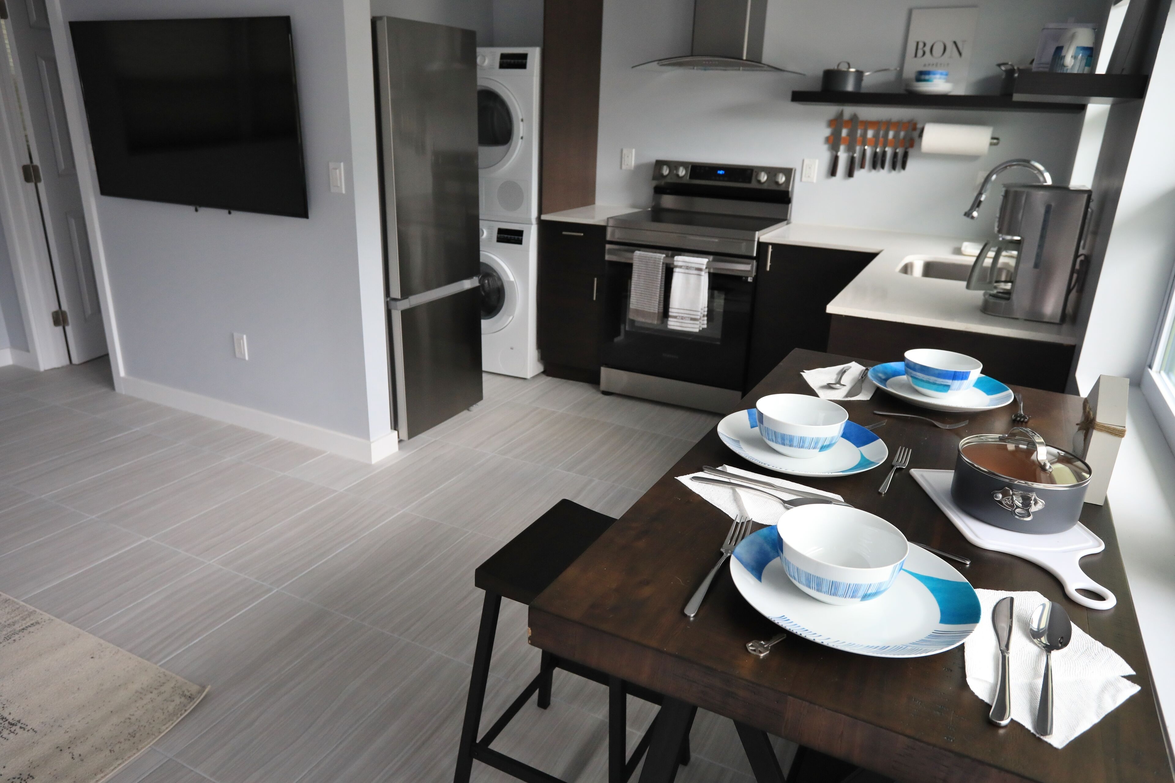 A modern kitchen with stainless steel appliances, a dining table set with plates, bowls, and cutlery.