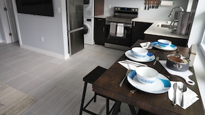 A modern kitchen with a built-in oven, microwave, and washing machine. There is a dining table set with plates, bowls, and cutlery.