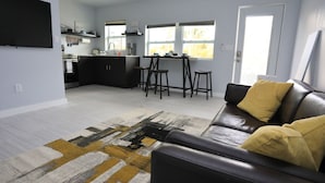 A modern living room with a black leather sofa, a patterned rug, and a kitchen in the background.