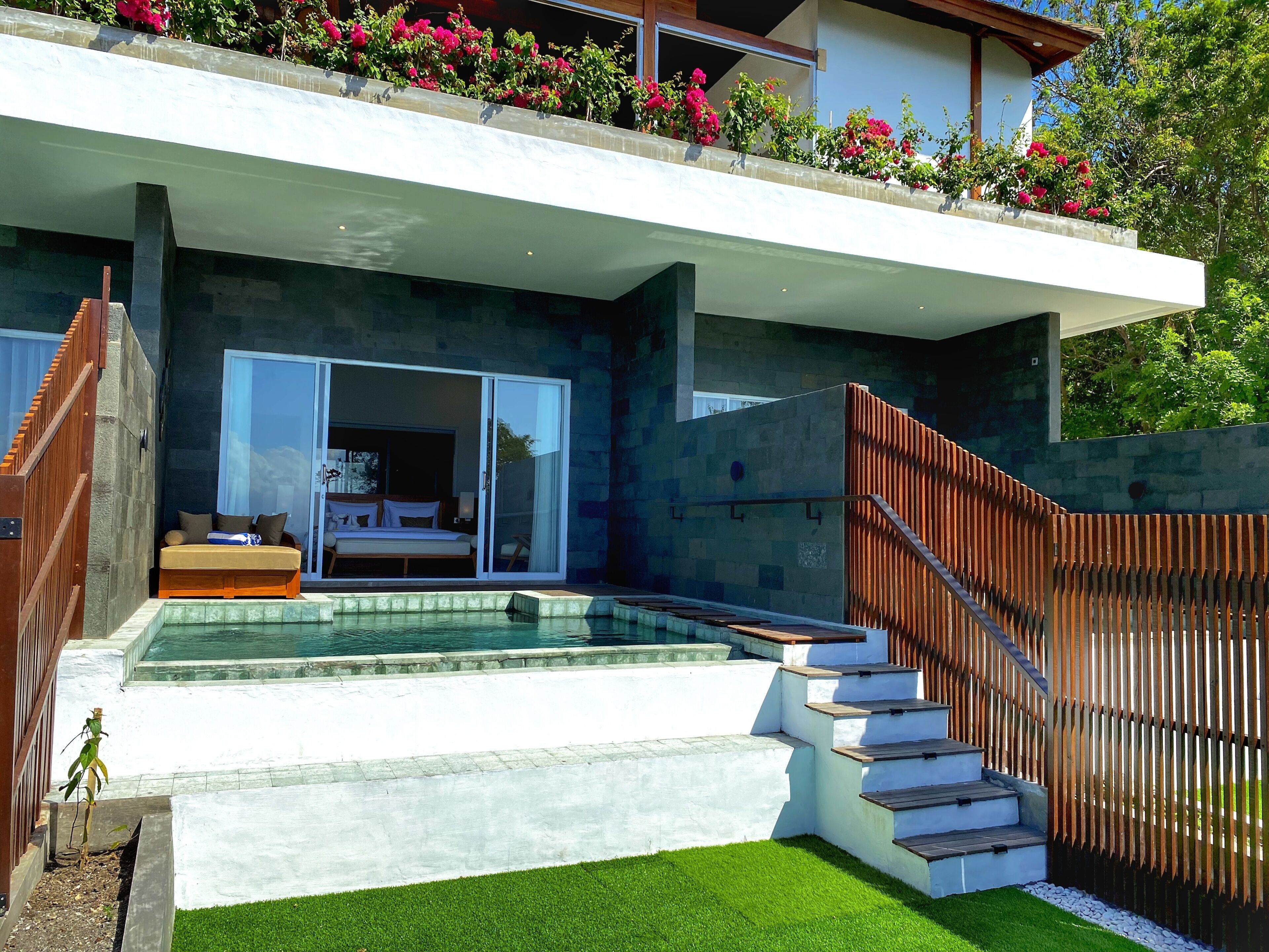 A modern house with a swimming pool, a balcony with flowers, and a staircase leading to the entrance.