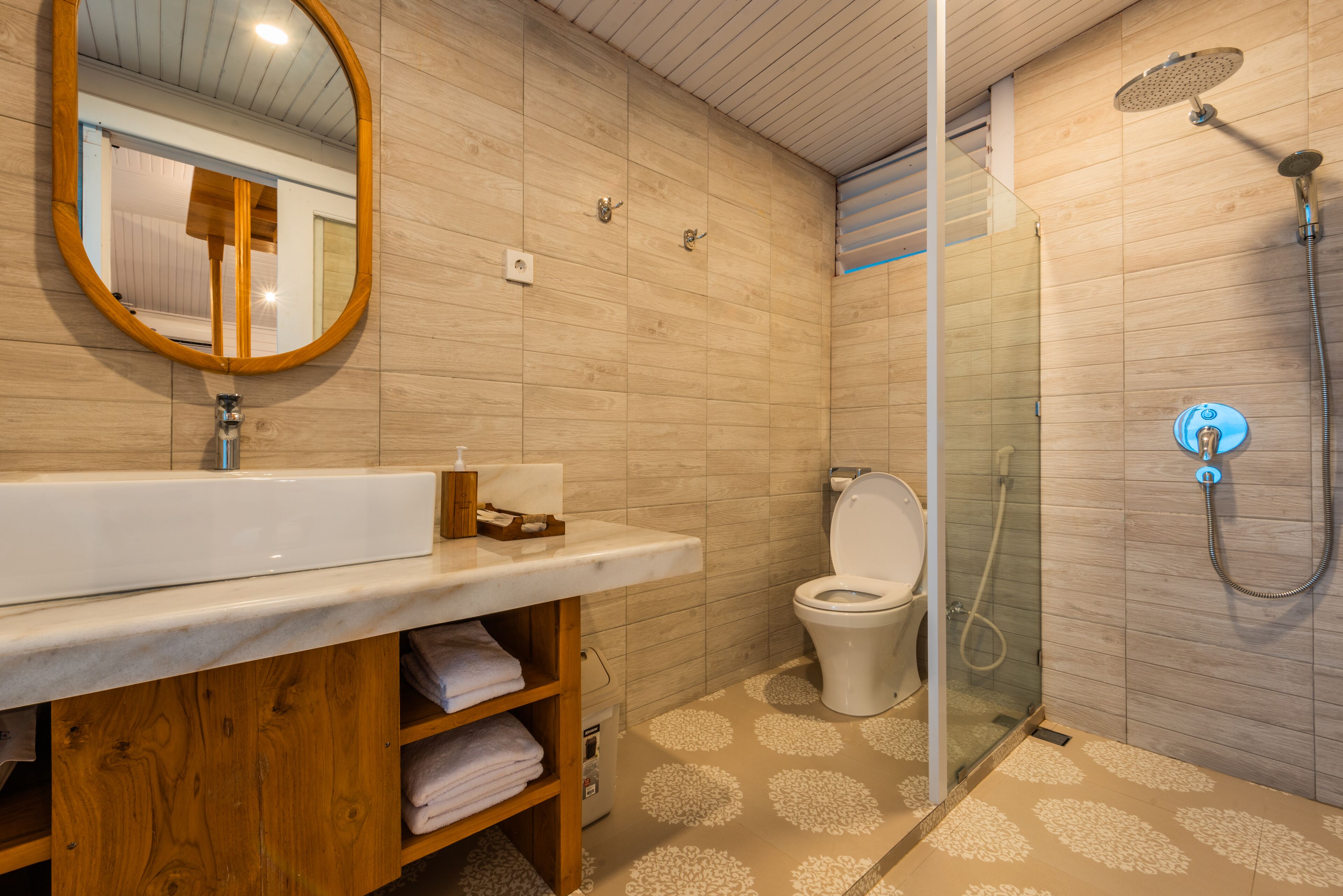A modern bathroom with a wooden vanity, a toilet, and a glass-enclosed shower area.