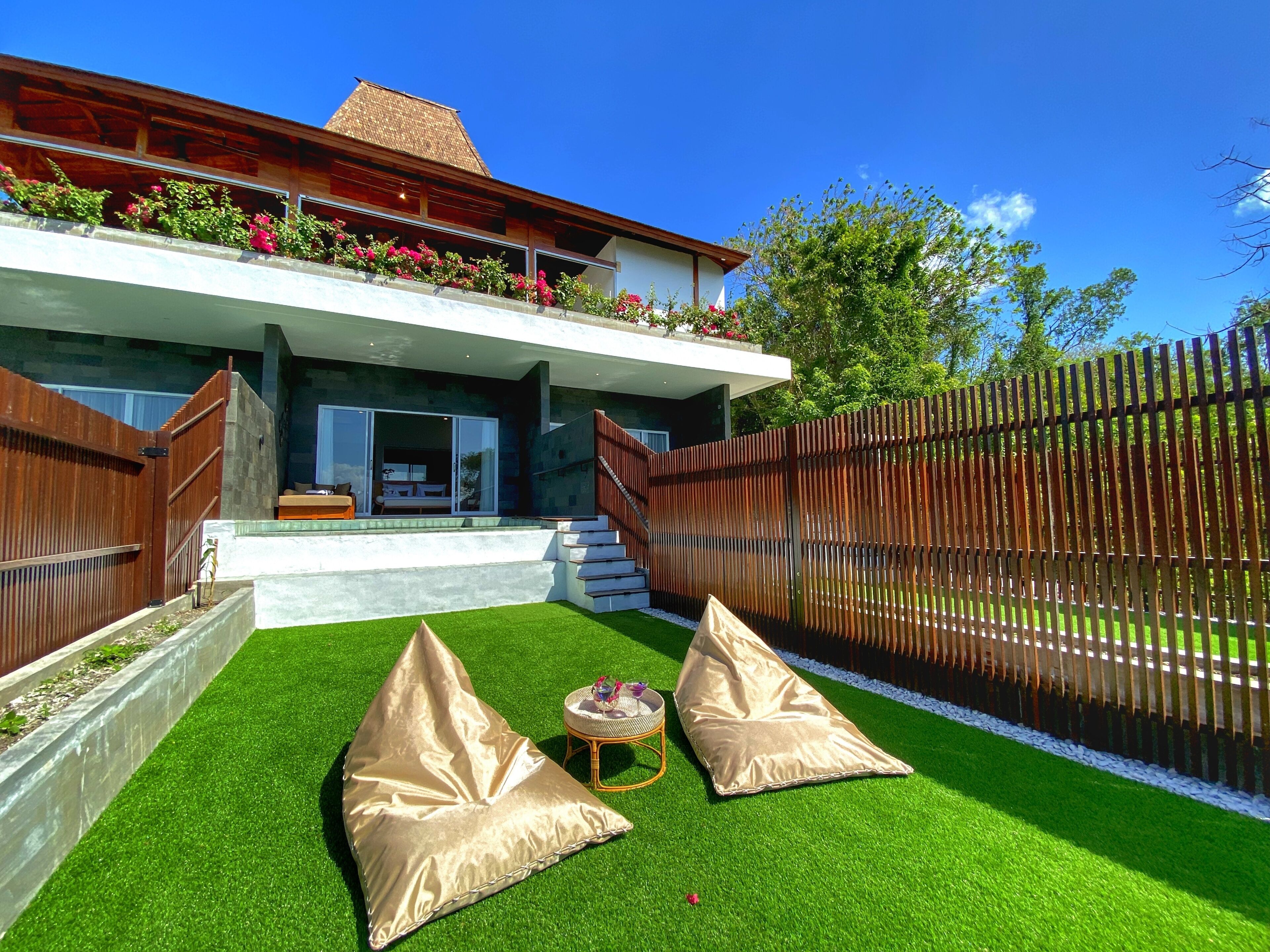 A modern house with a balcony, a wooden fence, and two beige cushions on artificial grass.