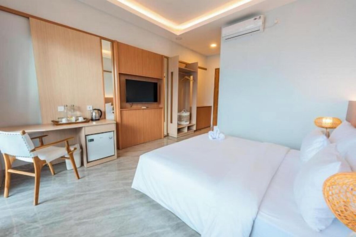 Una habitación de hotel con cama, escritorio, silla, televisión, armario y una kitchenette pequeña.