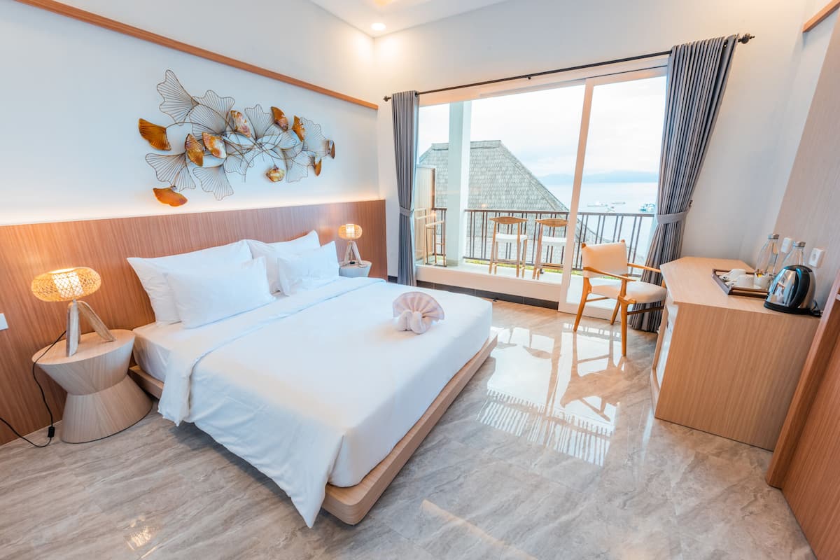 Ett modernt hotellrum med en stor säng, ett skrivbord och en balkong med utsikt över havet.