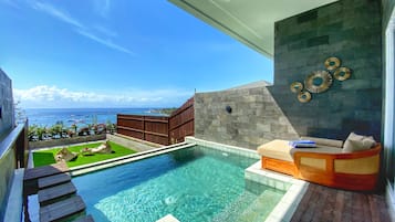 Une piscine à débordement moderne offrant une vue dégagée sur l’océan et les bateaux, une terrasse en bois et un coin salon confortable avec des coussins.