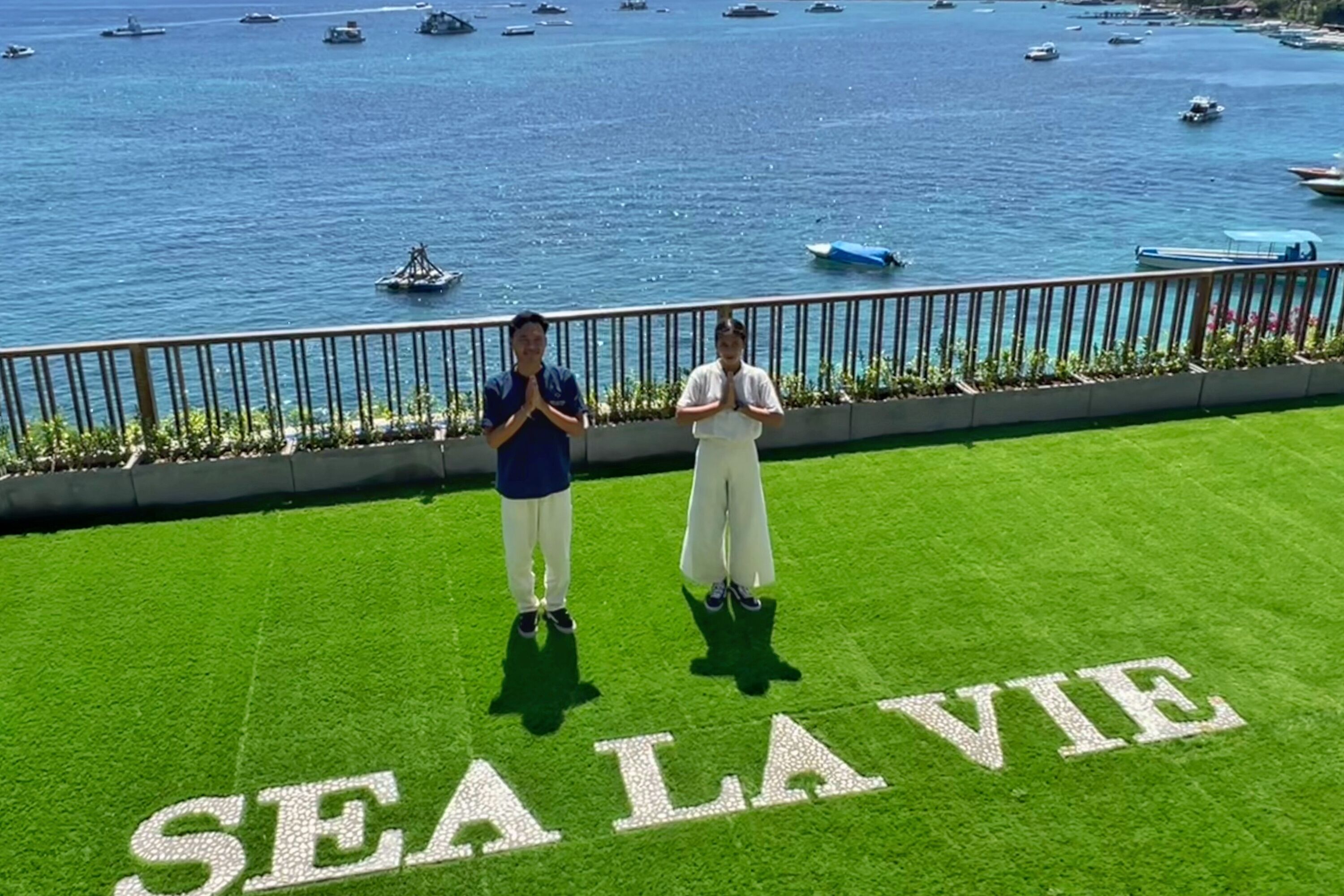 Deux personnes se tiennent sur une pelouse verdoyante, et les mots « SEA LAVIE » sont visibles au premier plan.