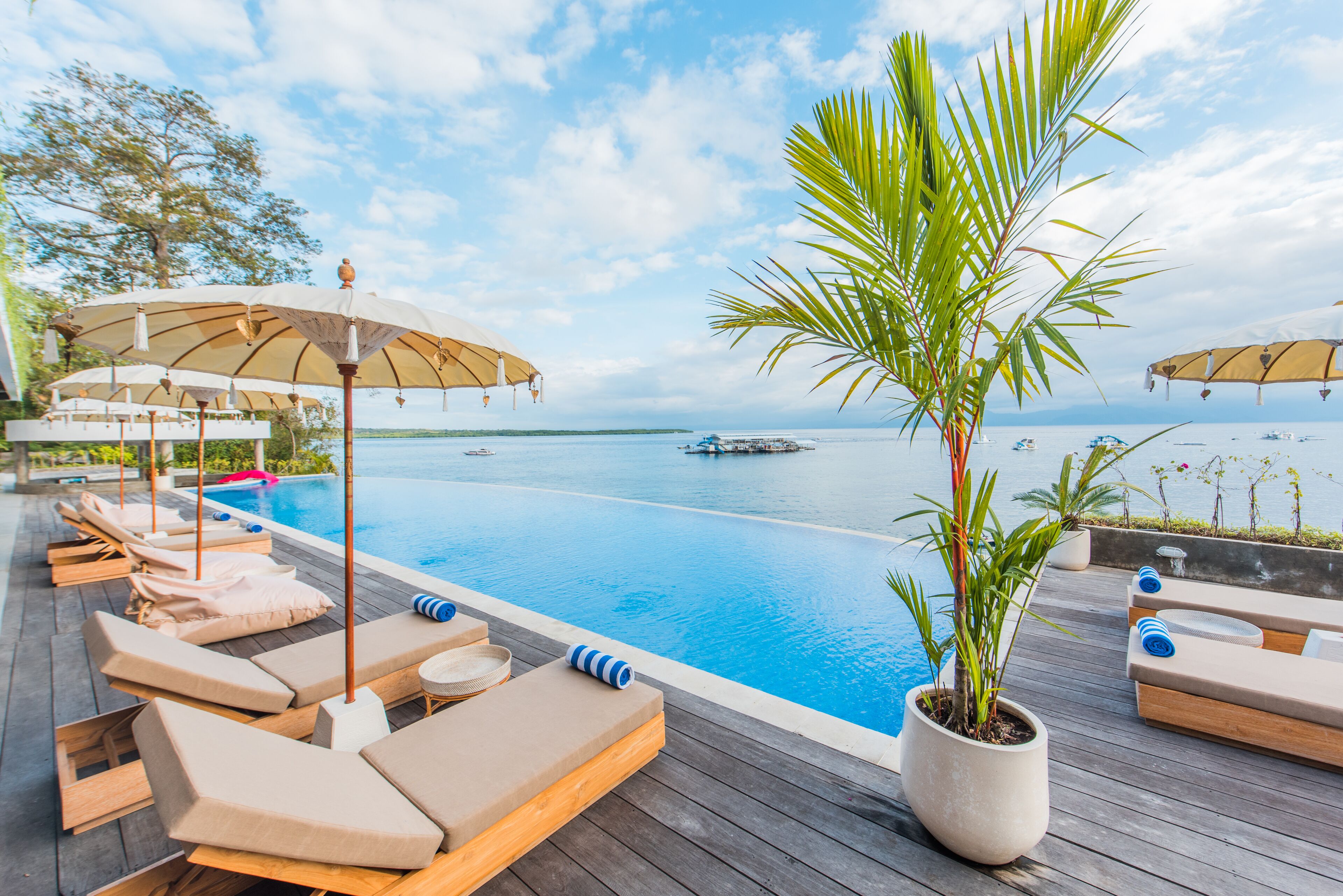 A poolside area with lounge chairs and umbrellas, a wooden deck, and a view of the sea.