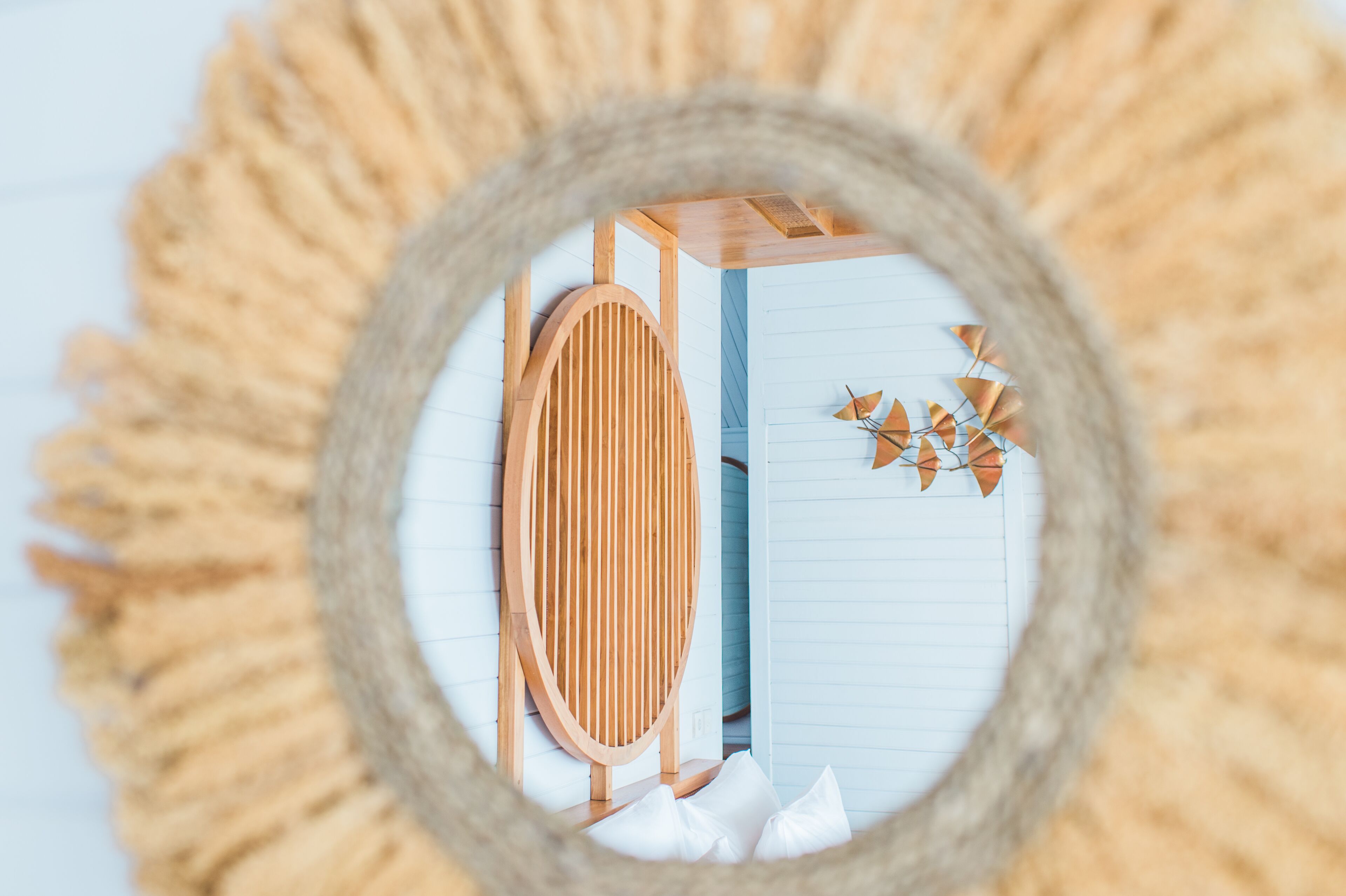 A circular mirror with a wooden frame reflecting a room with a wooden slat wall, a white door, and a small decorative item.