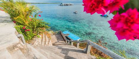 A staircase leading to a dock with clear blue water and boats in the distance.