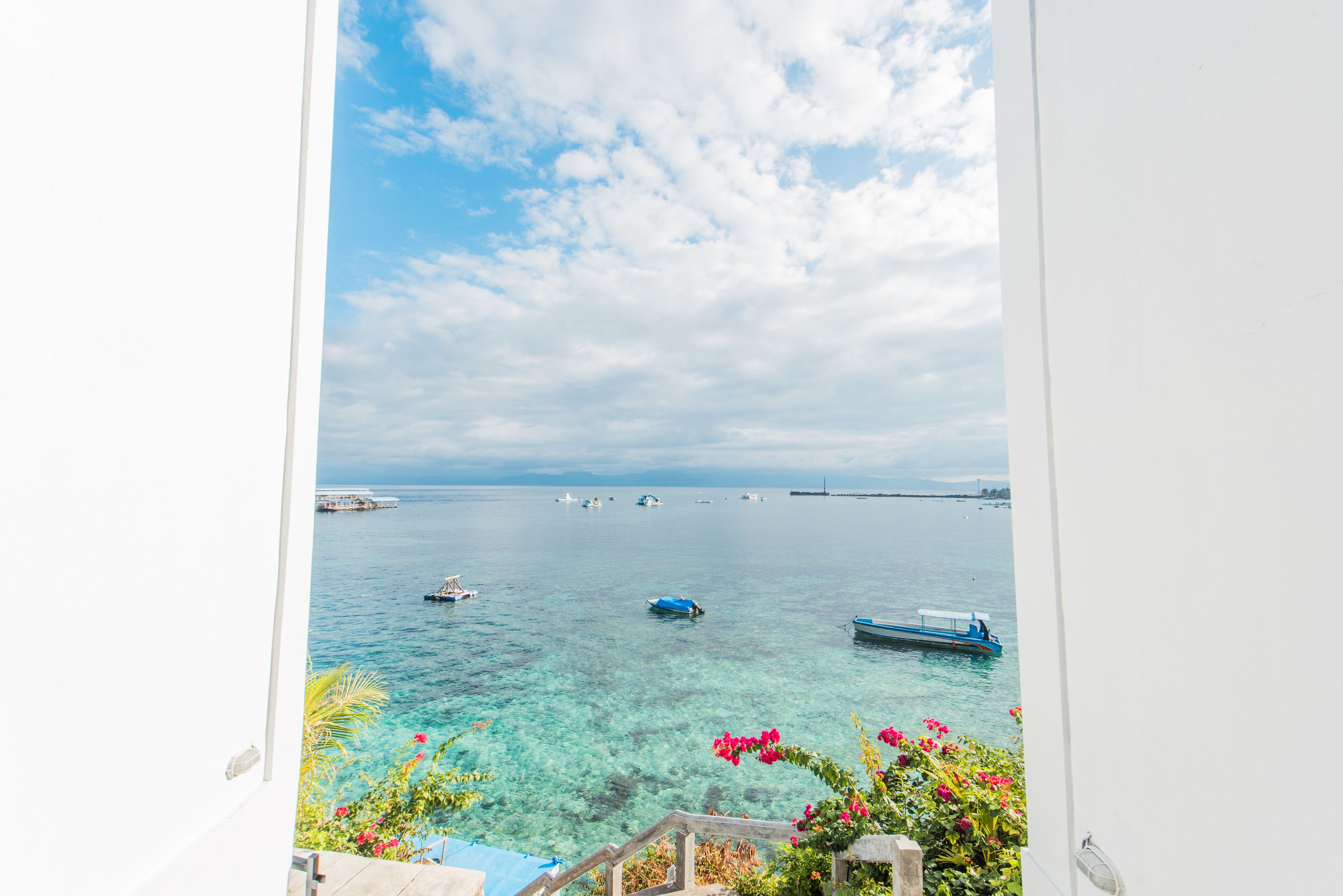 A coastal view from a balcony with clear water, boats, and a distant bridge.