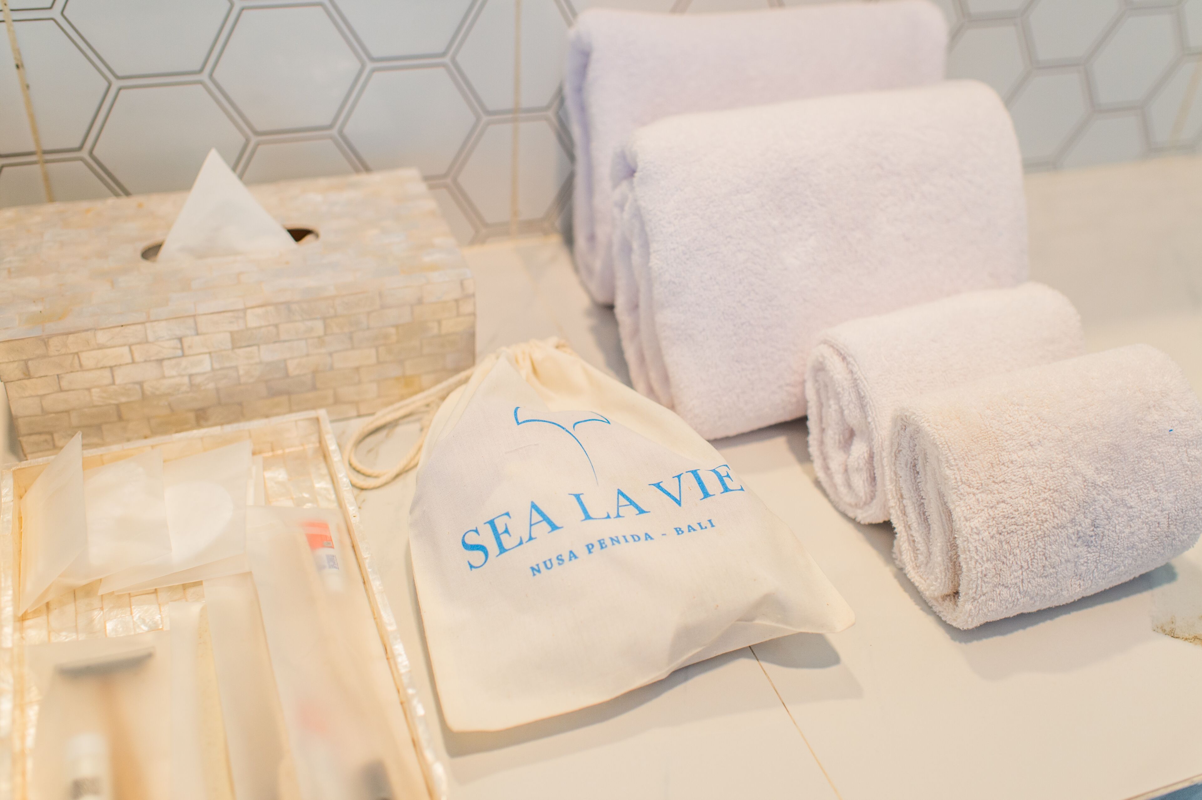 Une salle de bain avec un boîte de mouchoirs, des serviettes et un sac sur lequel est inscrit « SEA LA VIE ».