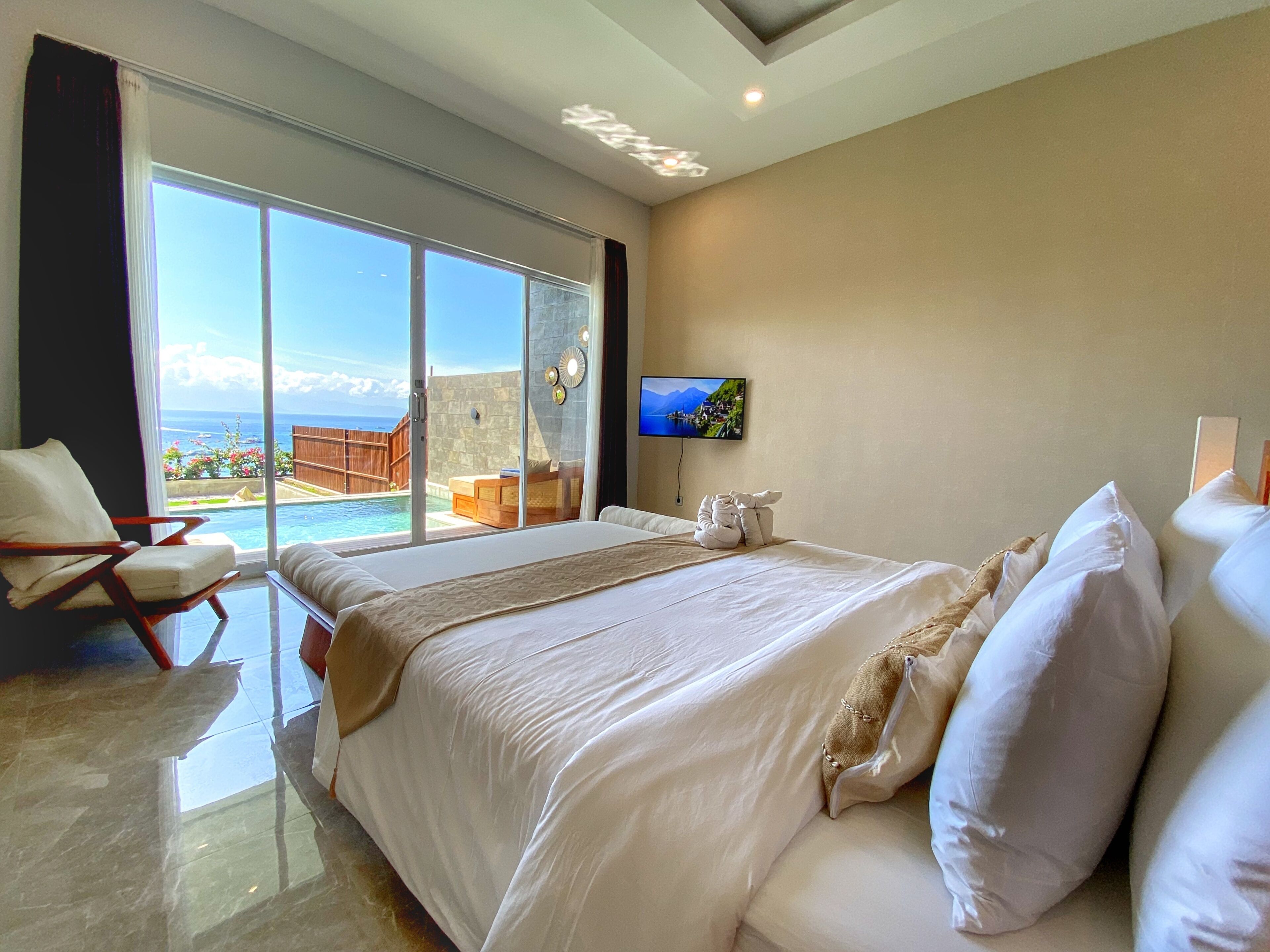 A spacious bedroom with a large bed, a TV, and a view of a pool and mountains.