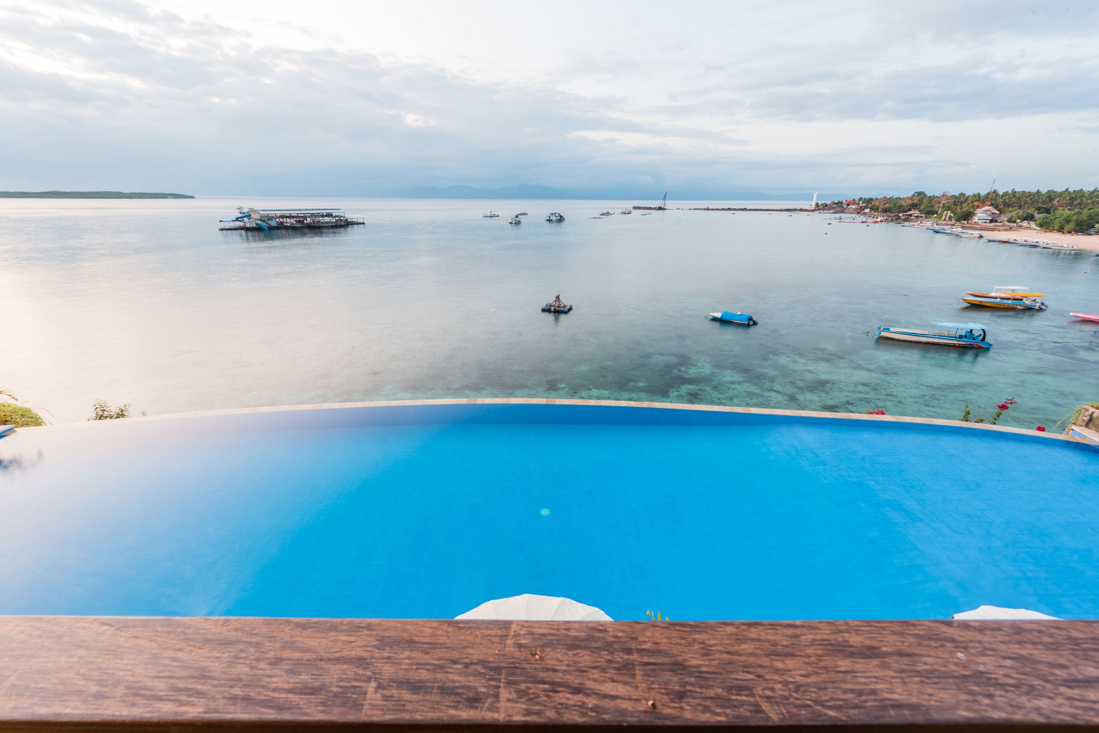 A view of a swimming pool with boats on the water and a distant shoreline.
