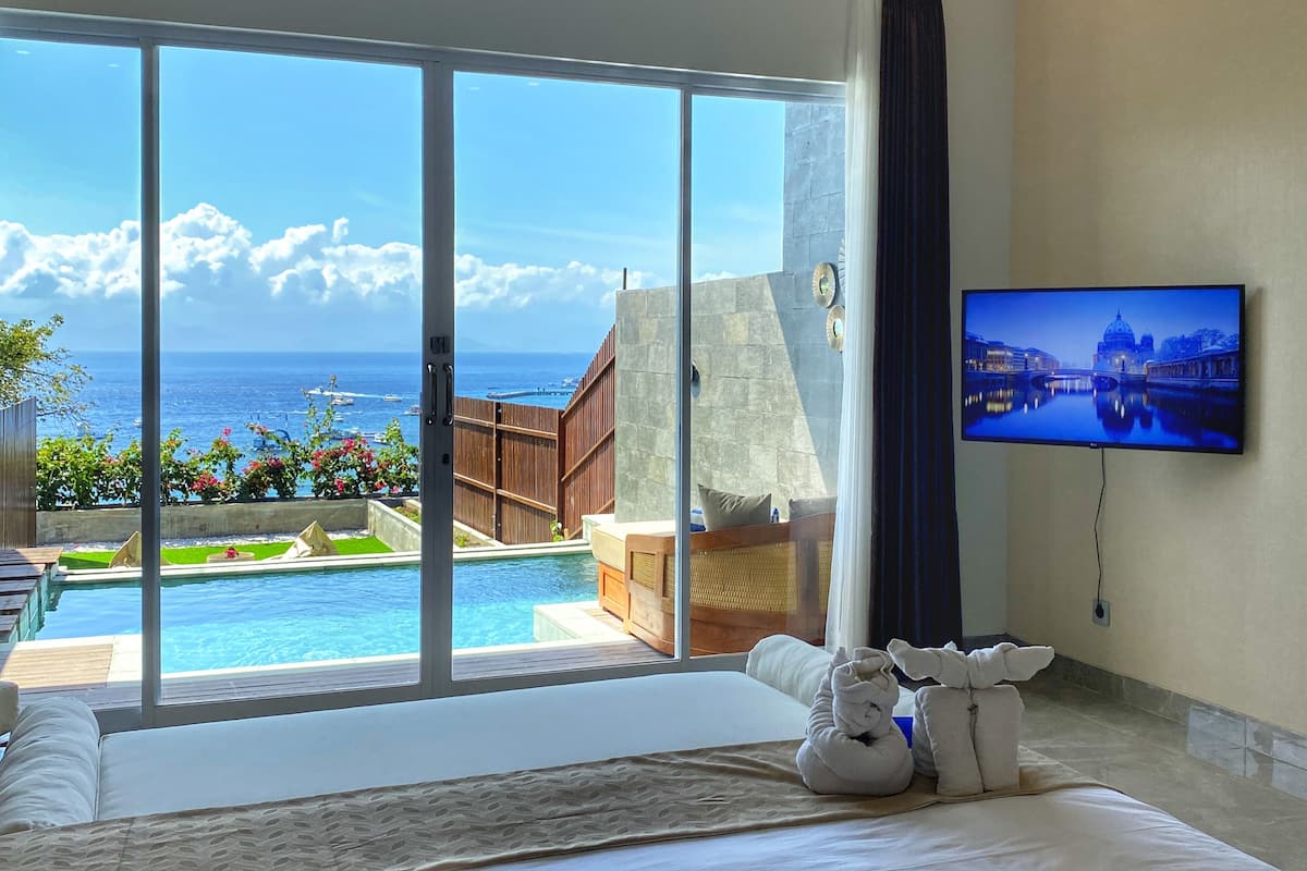 Ett hotellrum med en stor skjutdörr i glas som leder ut till en privat pool och en utsikt över havet.