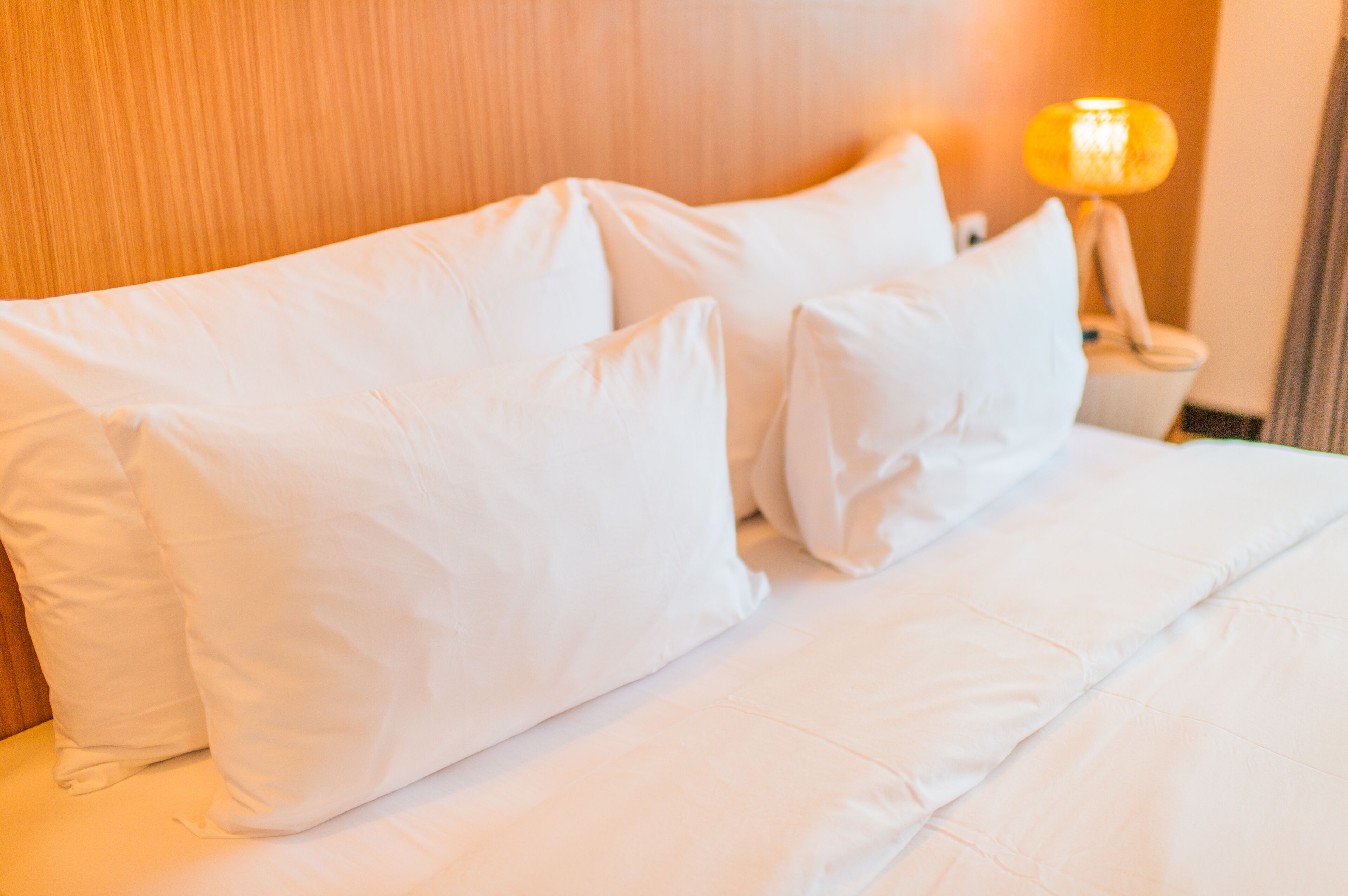 A bed with white bedding and pillows, a wooden headboard, and a bedside lamp.