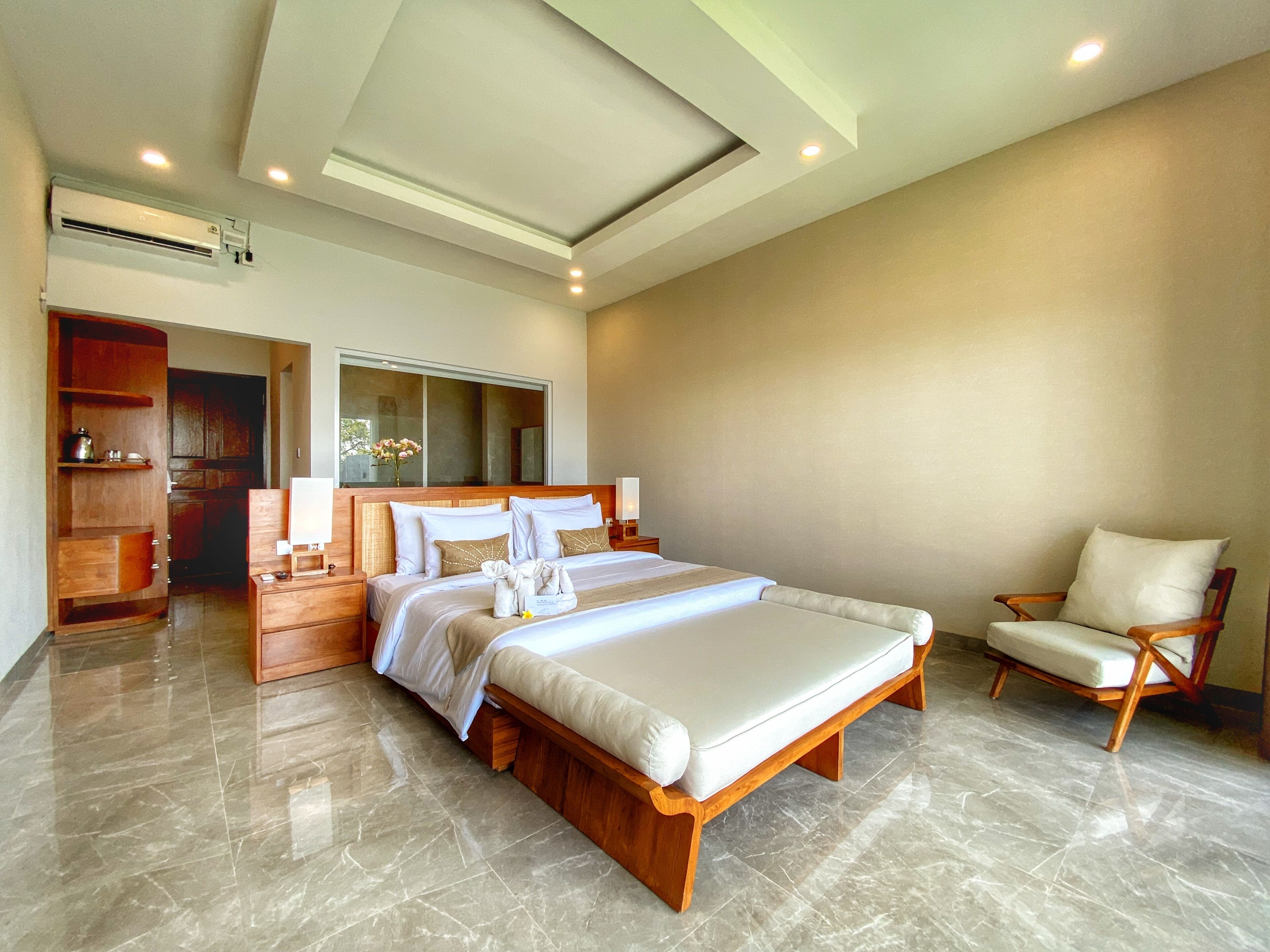 A spacious bedroom with a large bed, a wooden nightstand, a chair, and a bathroom visible through an open door.