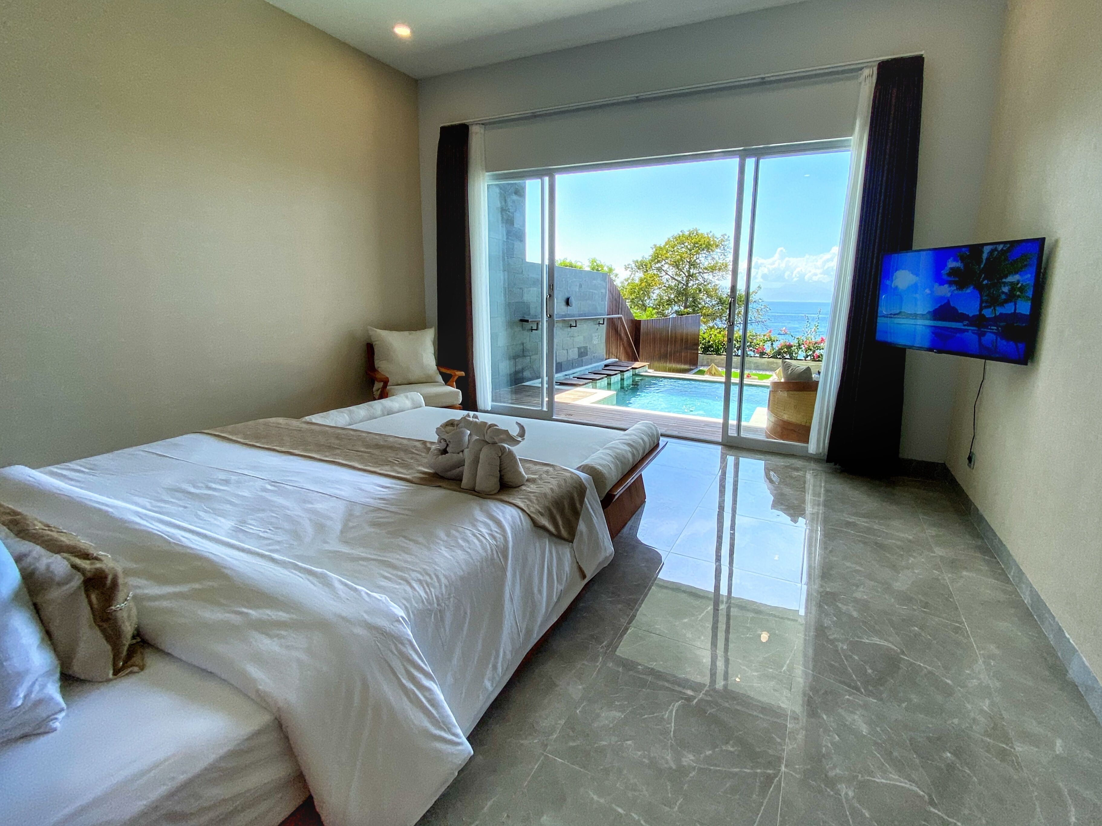 A hotel room with a large bed, a TV, and a view of a swimming pool and ocean.
