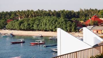 Una zona costera con barcos amarrados cerca de una playa arenosa, rodeada de abundante vegetación y edificios con tejados rojos.