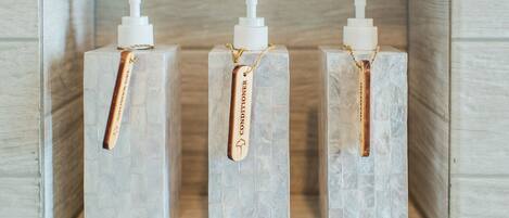 Three white bottles with pumps, each with a gold chain and a tag labeled "Conditioner," placed on a textured surface.