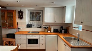A compact kitchen with white cabinets, a wooden countertop, a built-in oven, a dishwasher, and a window with lace curtains. - Vacation cottage Alte Kirchgasse (Zell (Mosel))