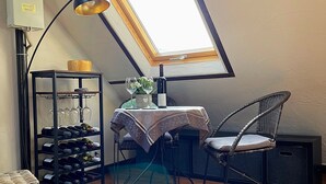 A cozy attic room with a slanted skylight, a table with a wine bottle and glasses, a wicker chair, and a wine rack. - Vacation cottage Alte Kirchgasse (Zell (Mosel))
