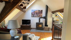 A cozy loft bedroom with a sloped ceiling, wooden beams, a fireplace, a television, and a view of the outdoors. - Vacation cottage Alte Kirchgasse (Zell (Mosel))