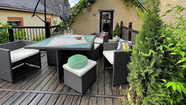 An outdoor patio with wicker furniture, a table with a placemat, and a small brick building with ivy. - Vacation cottage Alte Kirchgasse (Zell (Mosel))