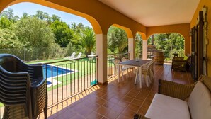 Un patio cubierto con piscina, mobiliario exterior y vistas de la vegetación circundante.