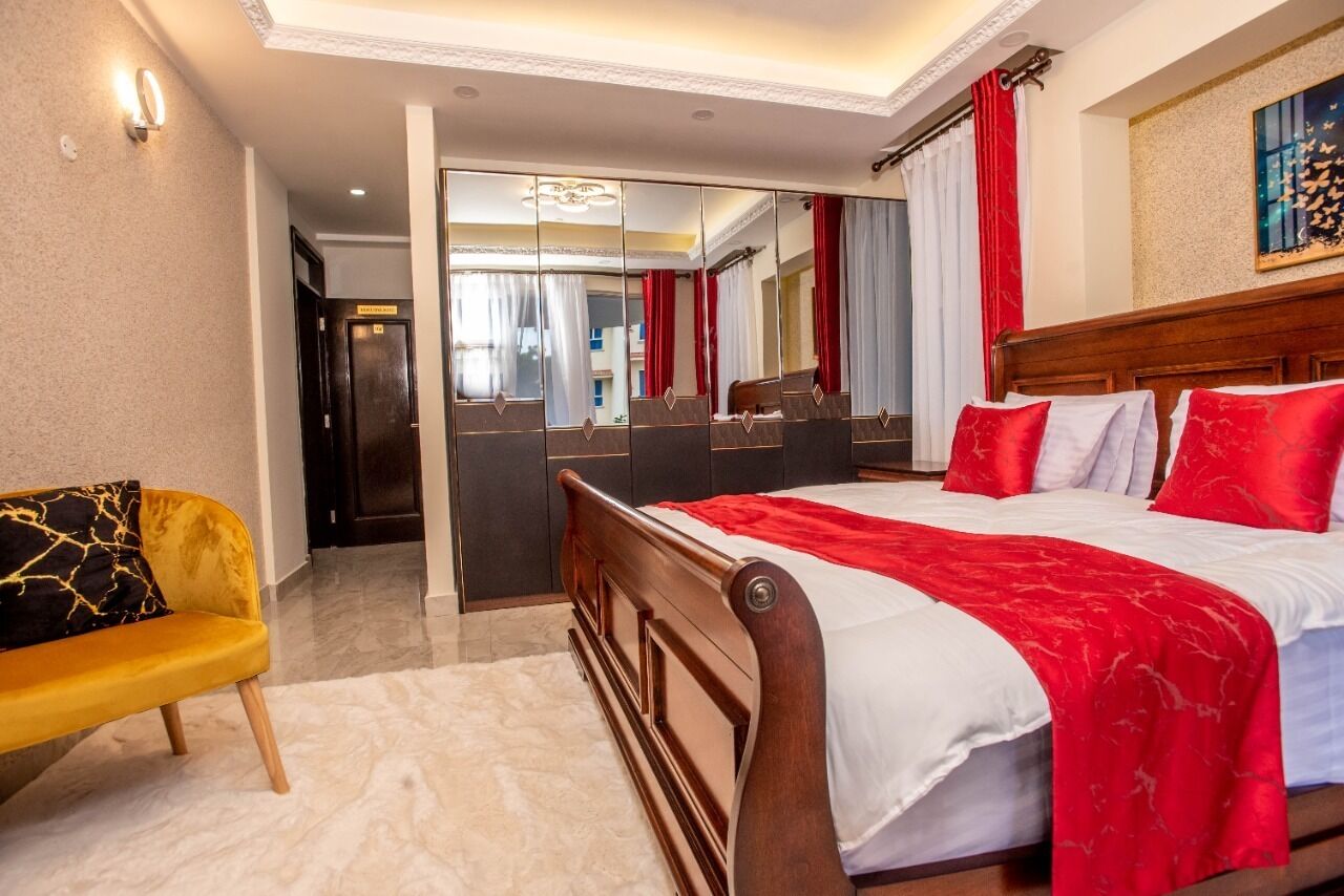 A hotel room with a large bed, a wooden headboard, a mirror, and a yellow sofa with a black and gold patterned cushion.