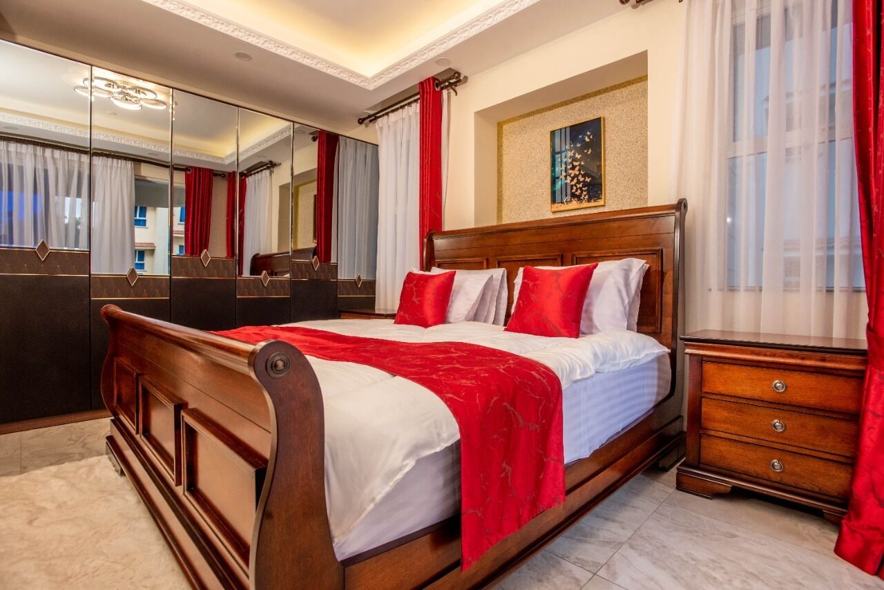 Een slaapkamer met een houten bed, rood-wit beddengoed, een grote spiegel en een dressoir.