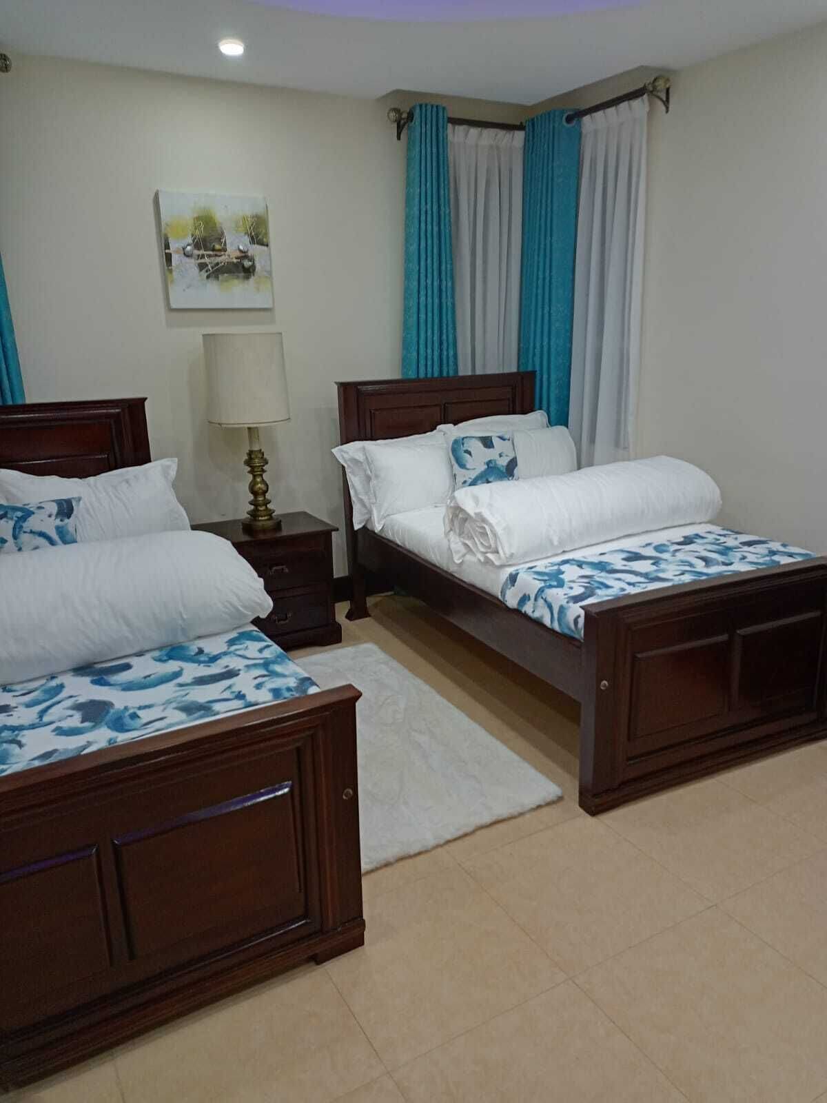 A hotel room with two wooden beds, a nightstand with a lamp, a white rug, and a painting on the wall.