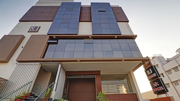 Un edificio moderno con techo plano, ventanas amplias y un letrero que indica “RJ Residency” y “Habitaciones con aire acondicionado”.