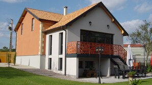 Una casa de dos pisos con balcón, chimenea y un pequeño espacio al aire libre con sillas y mesas.