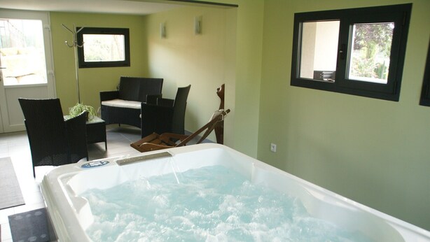 Una habitación con jacuzzi, mobiliario de mimbre y dos ventanas.