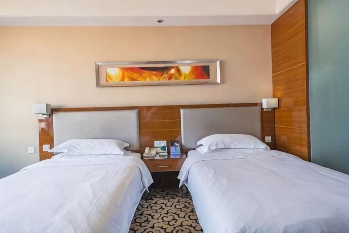 A hotel room with two beds, a nightstand, a lamp, and a painting on the wall.