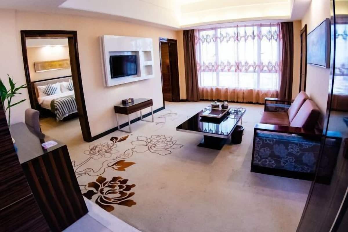 A hotel room with a flat-screen TV mounted on the wall, a sofa, a coffee table, and a large window with curtains.