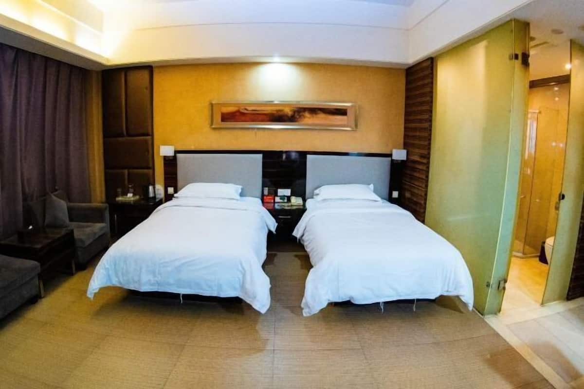 A hotel room with two beds, a sofa, a nightstand, and a painting on the wall.