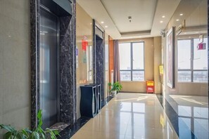 A hotel lobby with a marble reception desk, a glass elevator, and large windows offering a city view. - Xi’erdun Hotel (Gao'an)