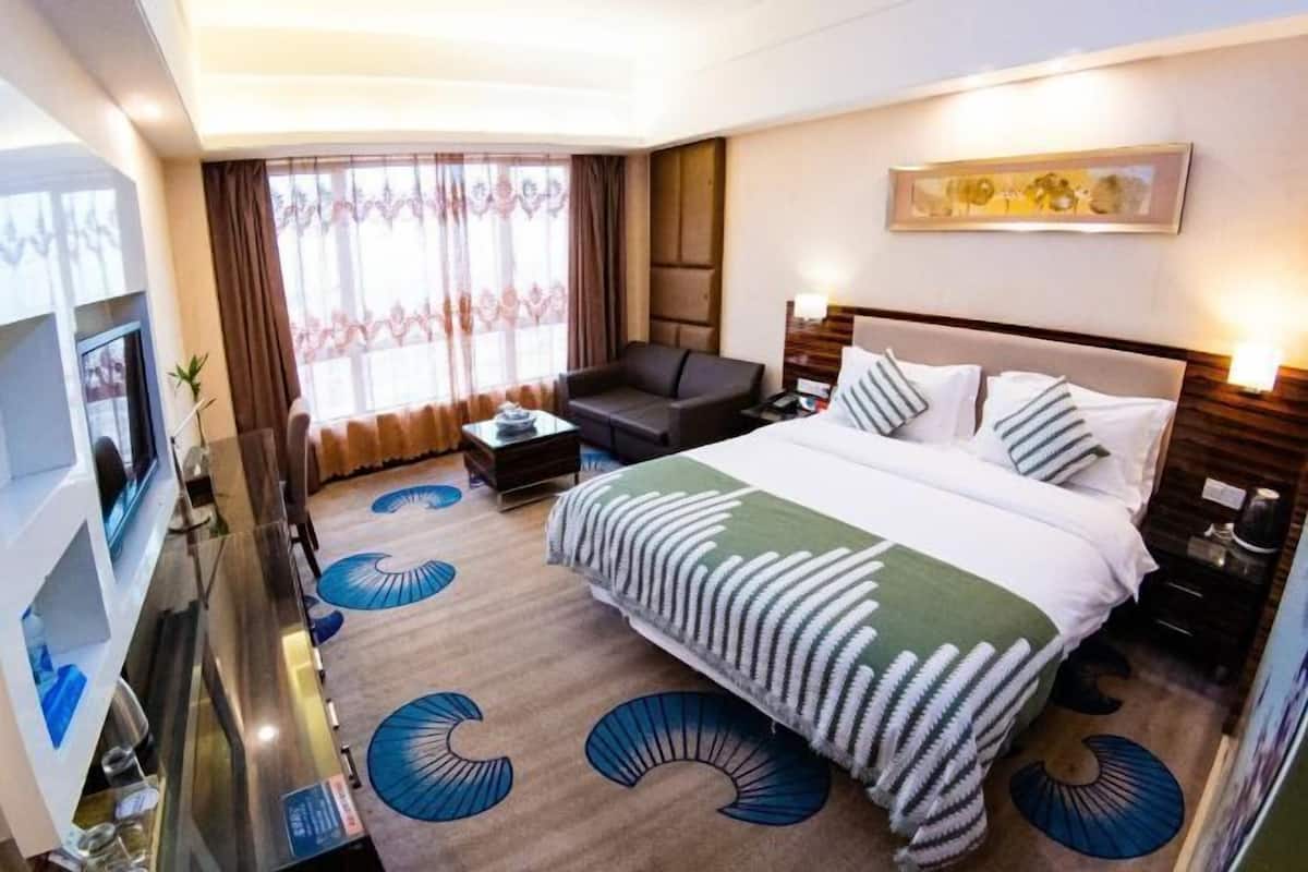 A hotel room with a large bed, a sofa, a TV, and a desk.