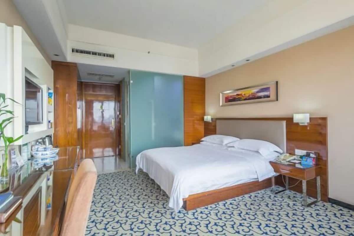 A hotel room with a bed, bedside table, lamp, and a painting on the wall.
