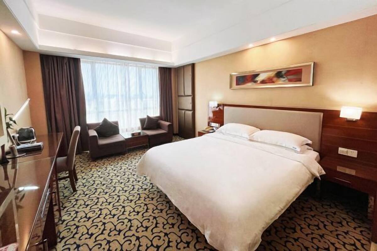 A hotel room with a large bed, a desk, a chair, a sofa, and a window with curtains.