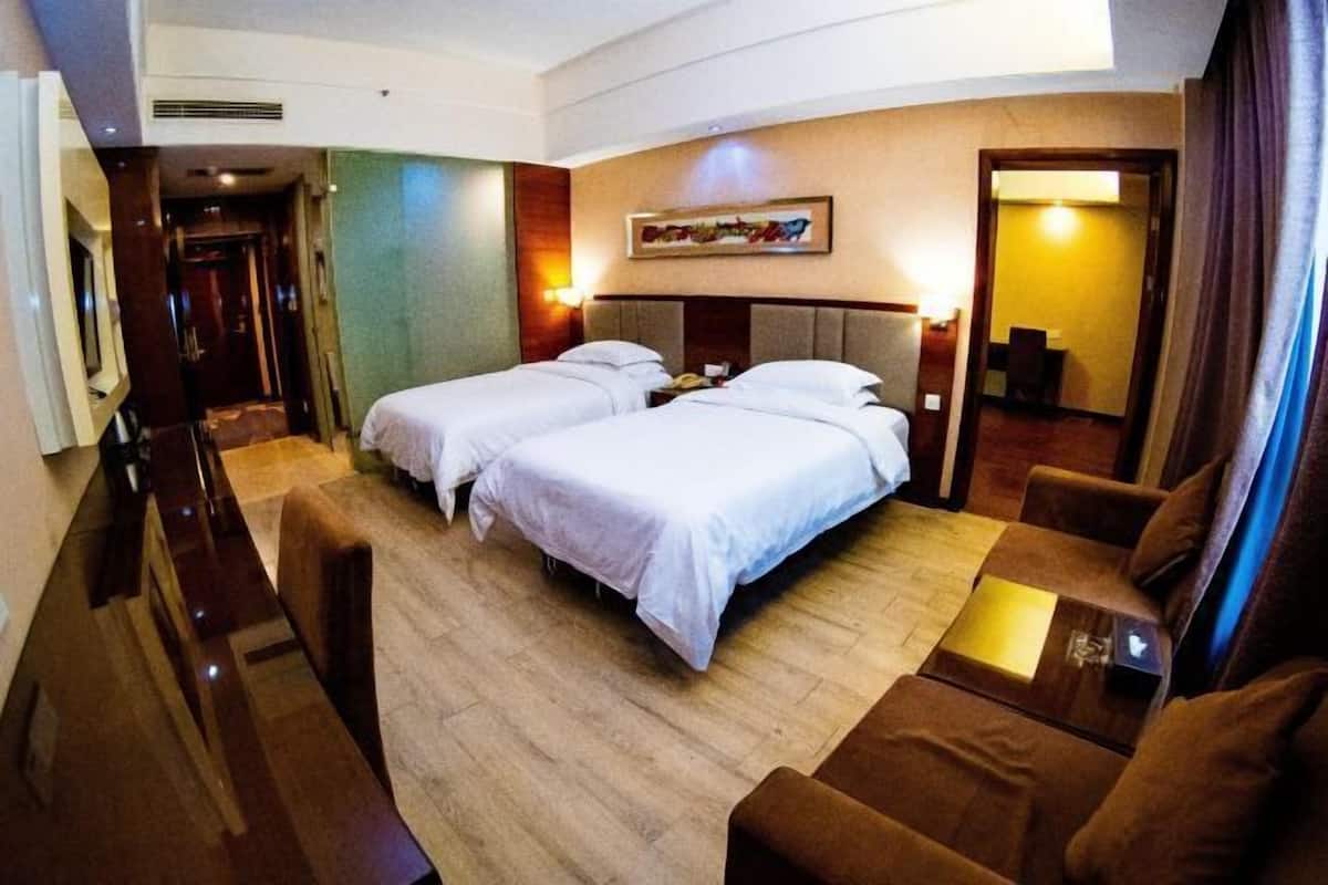 A hotel room with two beds, a sofa, a desk, and a painting on the wall.